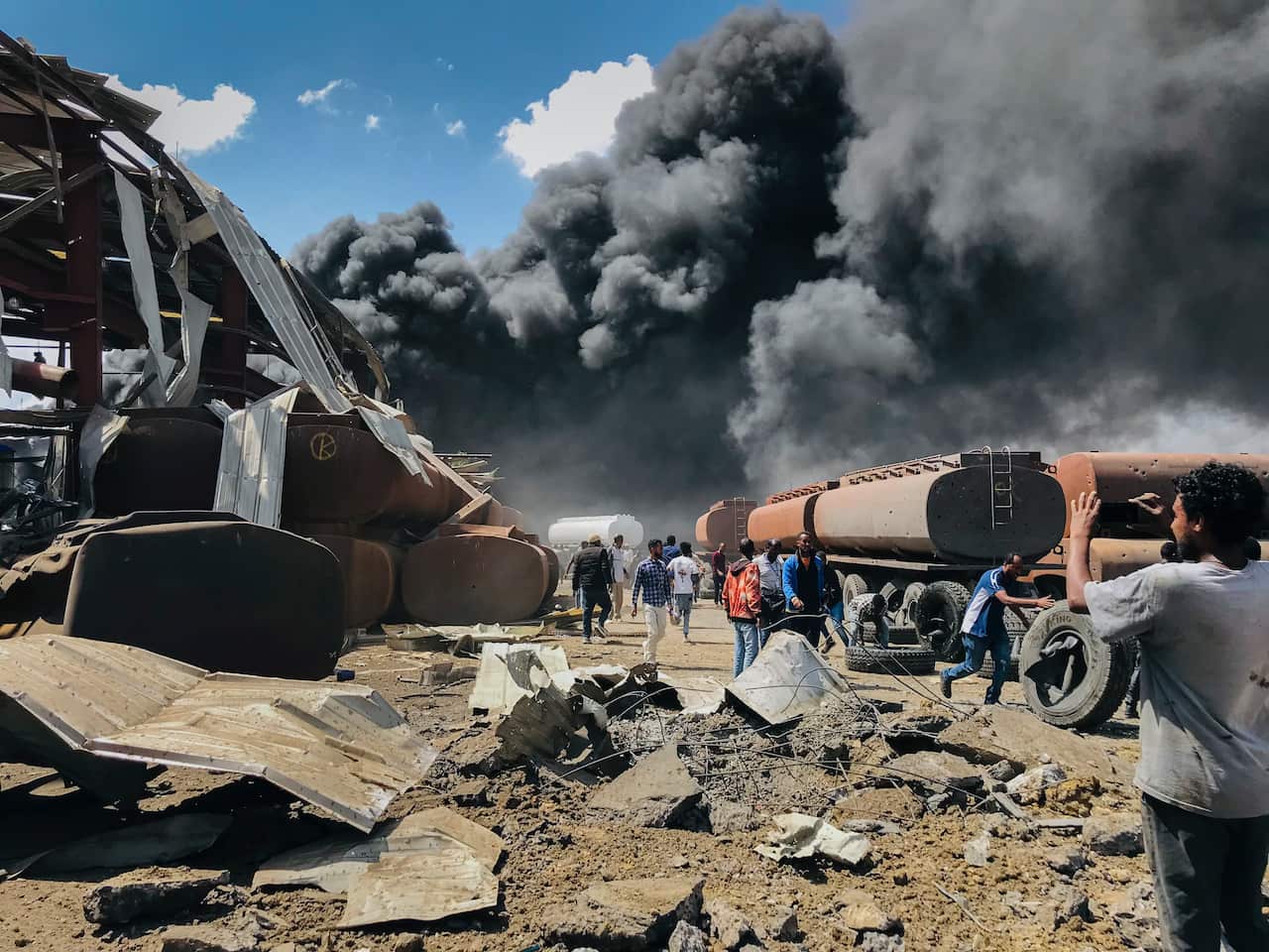 People are seen in front of clouds of black smoke from fires in the aftermath at the scene of an airstrike in Mekele, the capital of the Tigray region in 2021.