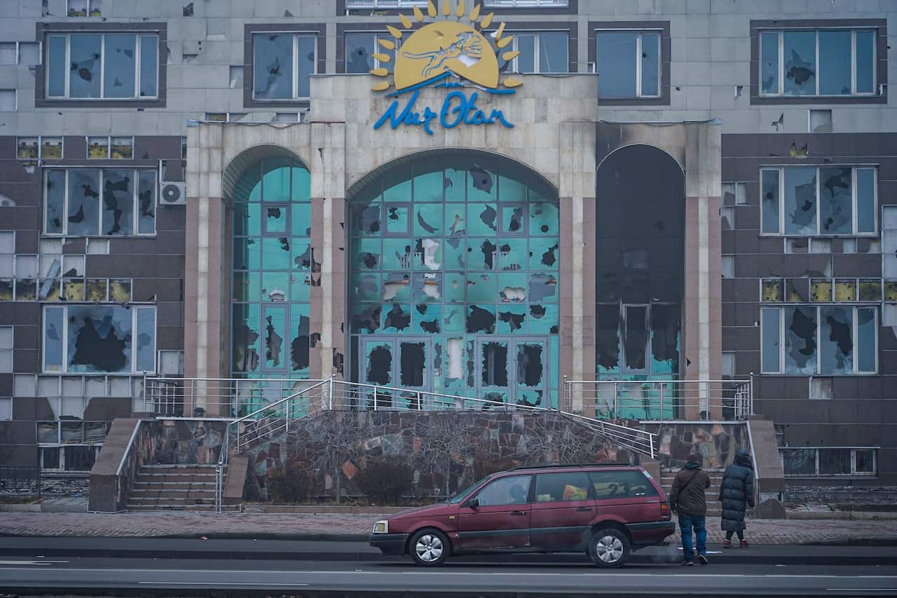 Kazakh people stand in from of damaged building during protests.
