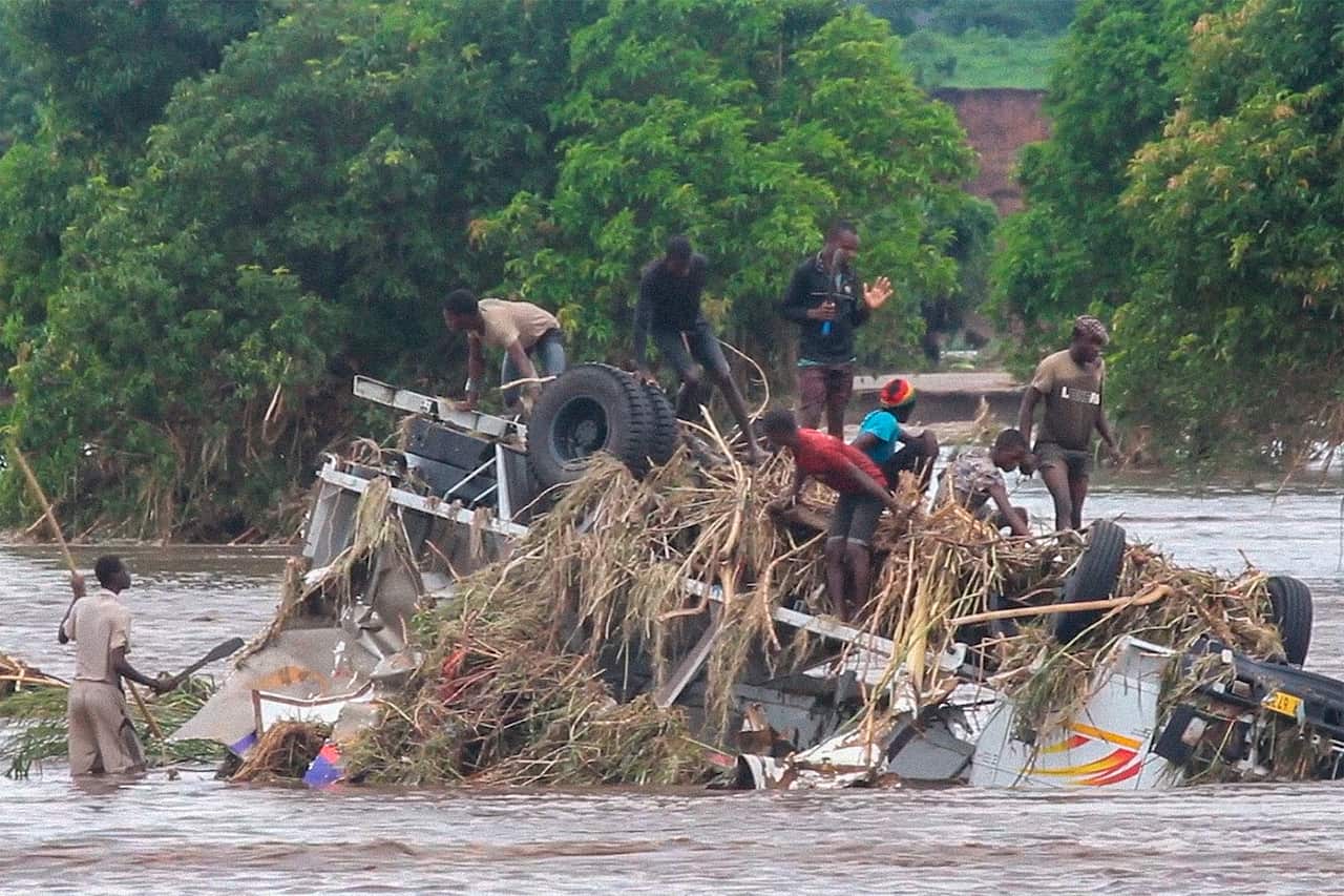 People stand on an overturned vehicle swept by flooding waters in Chikwawa, Malawi.