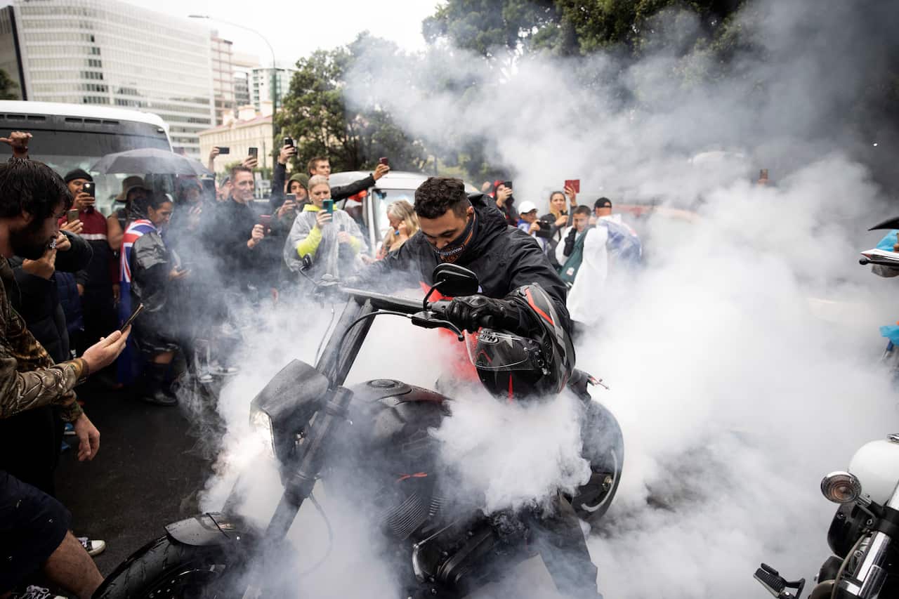 Protesters watch as a man spins the tire on his motorcycle in wet conditions as they demonstrate their opposition to coronavirus vaccine mandates.