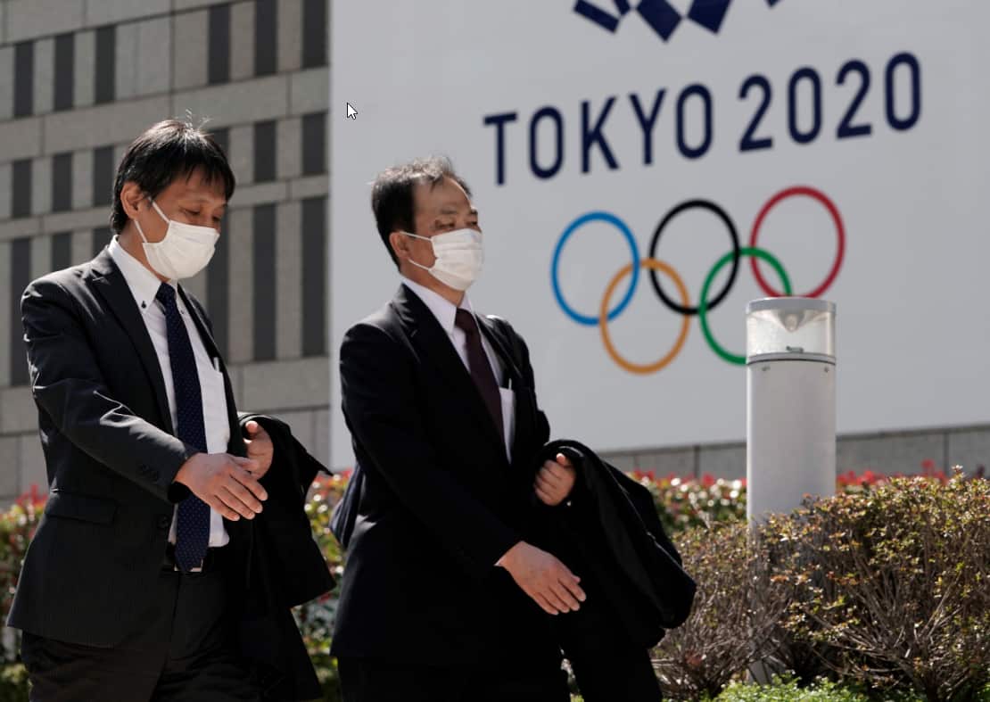 Office workers wearing masks walk past the emblem of Tokyo 2020 Olympics.