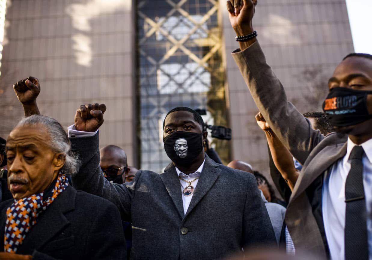 Brandon Williams wears a mask and pendant with the image of his uncle, George Floyd, and raises his fist at the courthouse in Minneapolis, Minnesota.