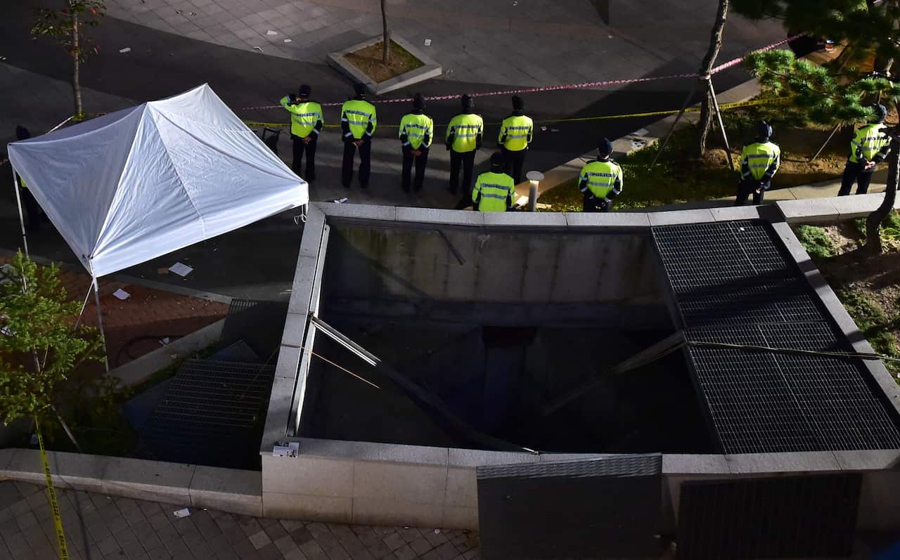 Policemen stand guard near a broken ventilation grate after concert goers fell through it into an underground parking area below in Seongnam City (Getty)
