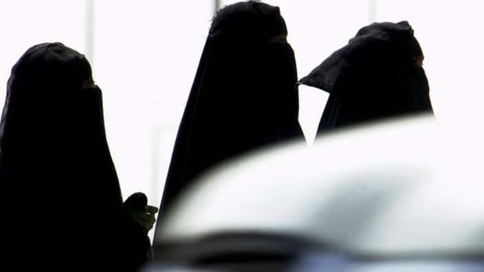 Saudi women walk past cars in a Riyadh, Saudi Arabia