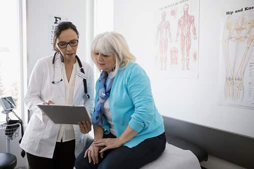 Female doctor and senior patient reviewing medical chart in clinic examination room
