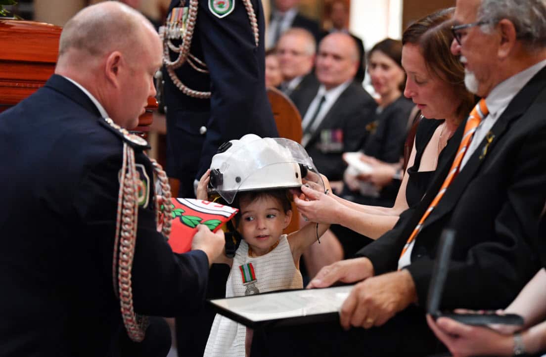 Charlotte O'Dwyer, the young daughter of RFS volunteer Andrew O'Dwyer receives her father's helmet by RFS Commissioner Shane Fitzsimmons.