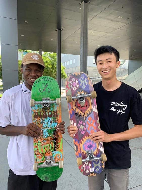 Keire Johnson (left) and Bing Lieu (right) hold skateboards promoting the message 'Consent is Rad.'
