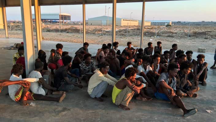 Rescued migrants sit on a coast some 100 kilometers (60 miles) east of Tripol