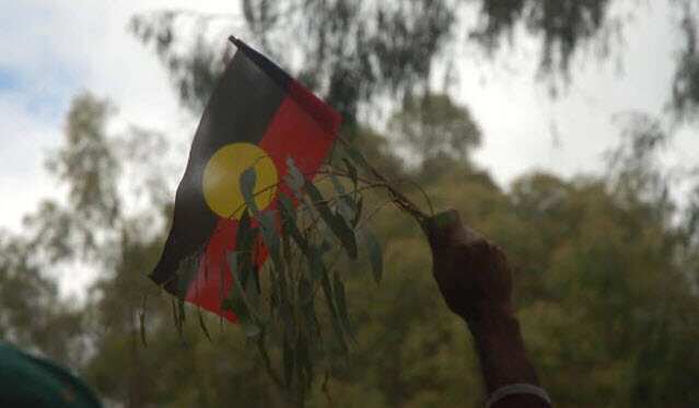 An Indigenous Australian holds up the Aborignal flag.