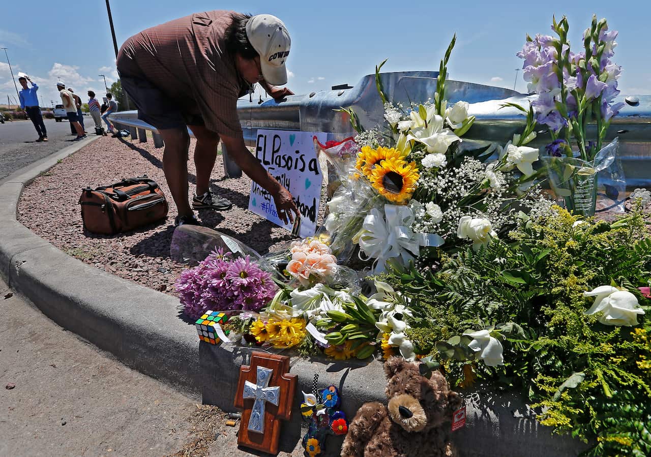 A man tapes a card to a sign next to a make shift memorial along the street behind the scene of a mass shooting at a Walmart in El Paso