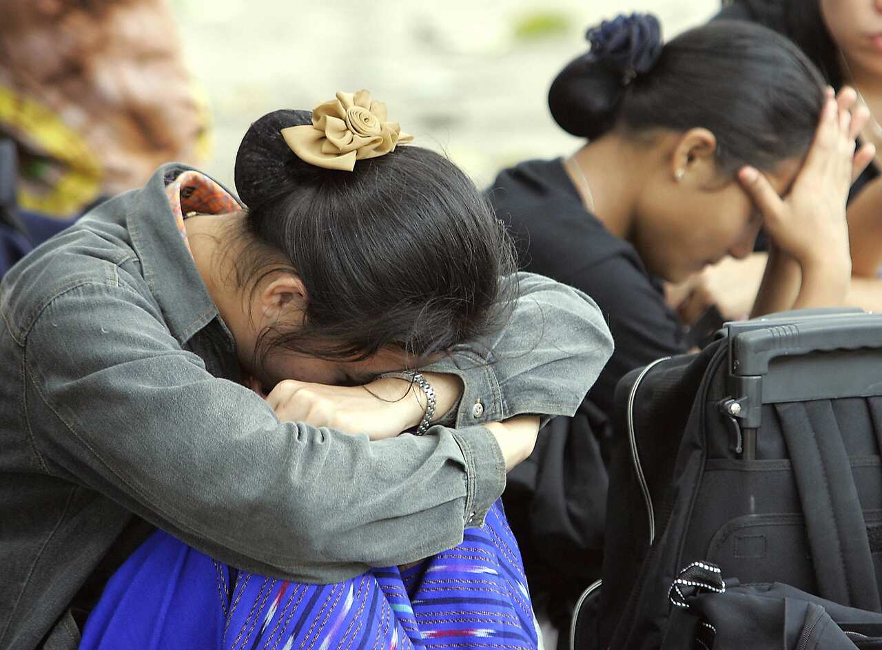 Two women with their faces covered by their hands are sitting. 