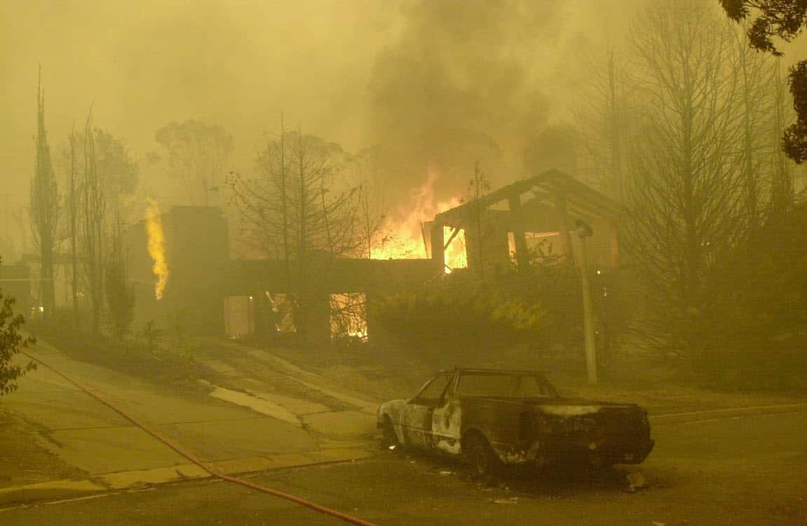 A burnt out car in the driveway as a house in the Canberra suburb of Torrens goes up in flames in 2003 (AAP)