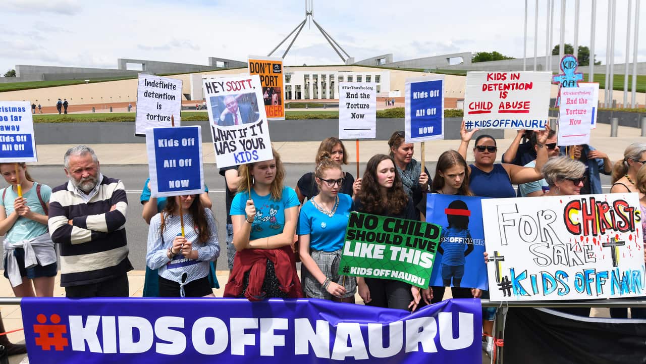 Protesters hold up signs during a rally demanding the resettlement of kids held on Nauru.