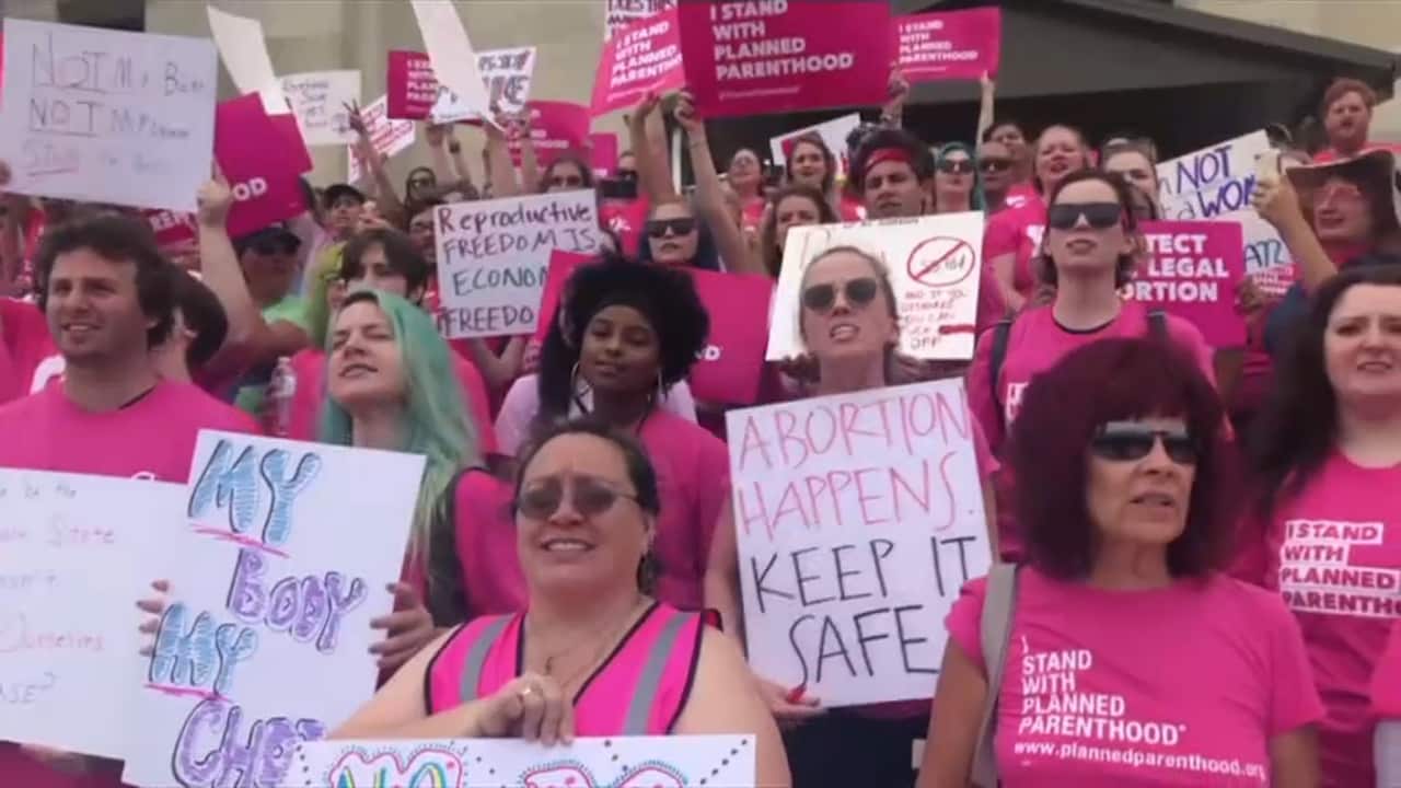 A group of people wearing pink shirts and holding placards