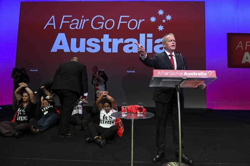 A group of protester sat down behind Mr Shorten as he took to the stage and started his speech.