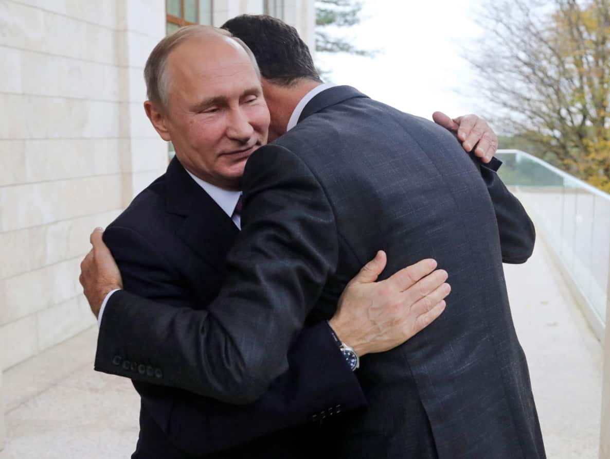 In this Monday, Nov. 20, 2017, photo, Russian President Vladimir Putin, left, embraces Syrian President Bashar Assad in the Bocharov Ruchei 