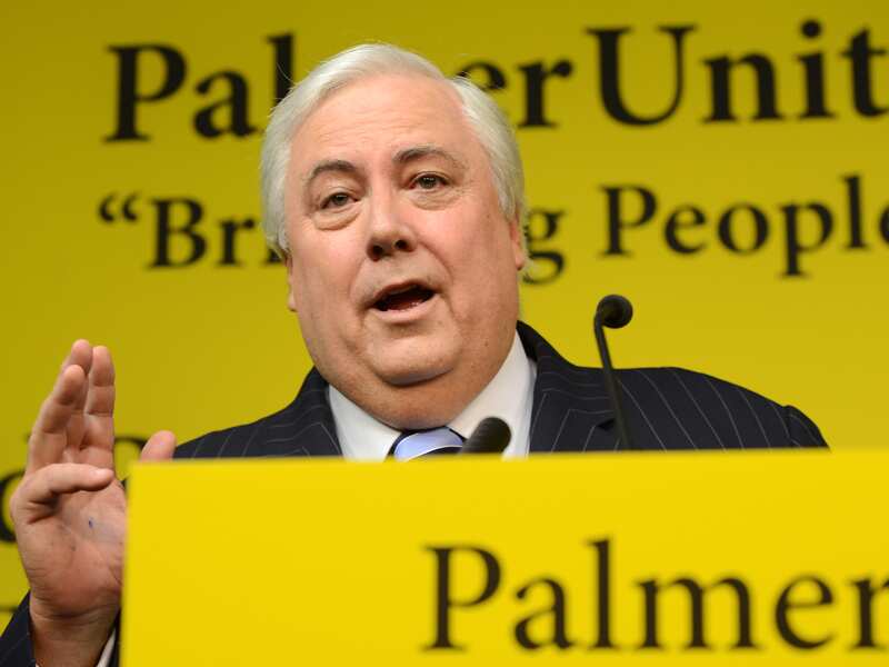 Clive Palmer speaking at podium with the yellow colours of the United Australia Party behind him. 