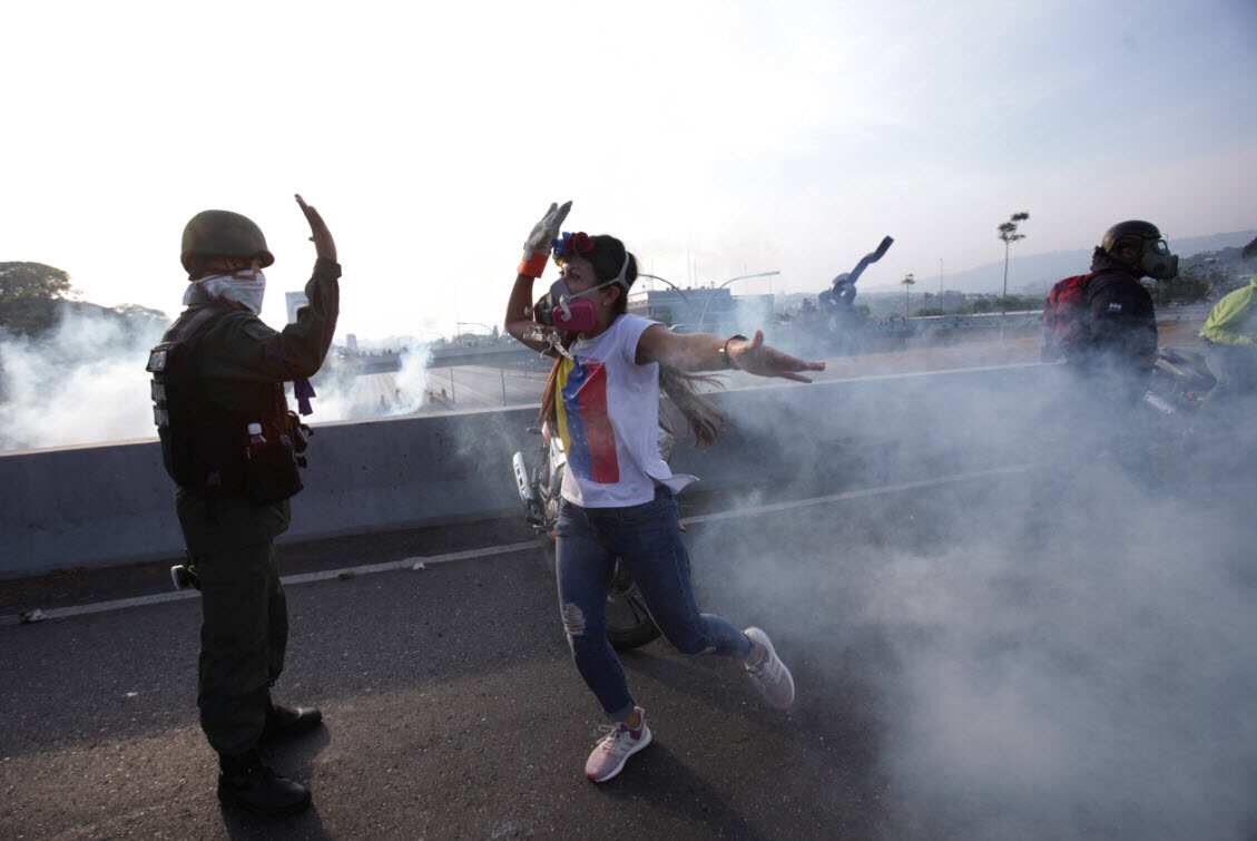 An opponent to Venezuela's President Nicolas Maduro high fives a rebel soldier on a highway overpass outside La Carlota air base amid tear gas fired by loyalist soldiers (AAP)