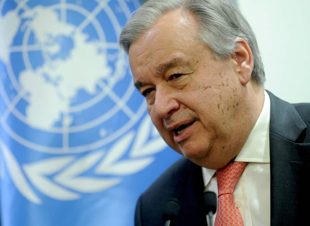 António Guterres wearing a suit in front of a UN flag.