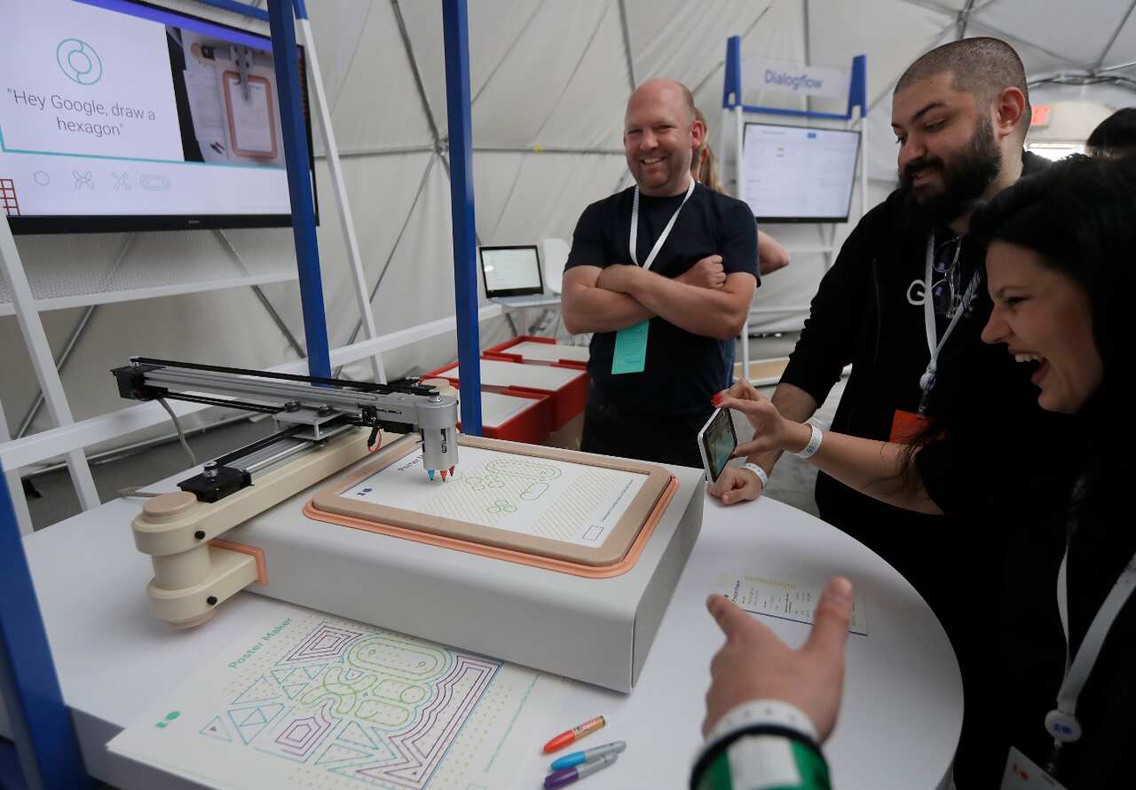 A group of people watch as a Google Assistant software development kit poster maker draws on voice command at the Google I/O conference in Mountain View