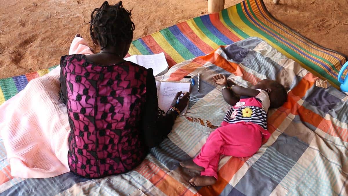 Atem*, 15, at home doing her school work in Dadaab, Kenya, while her 11-month-old daughter, Atol*, sleeps.
