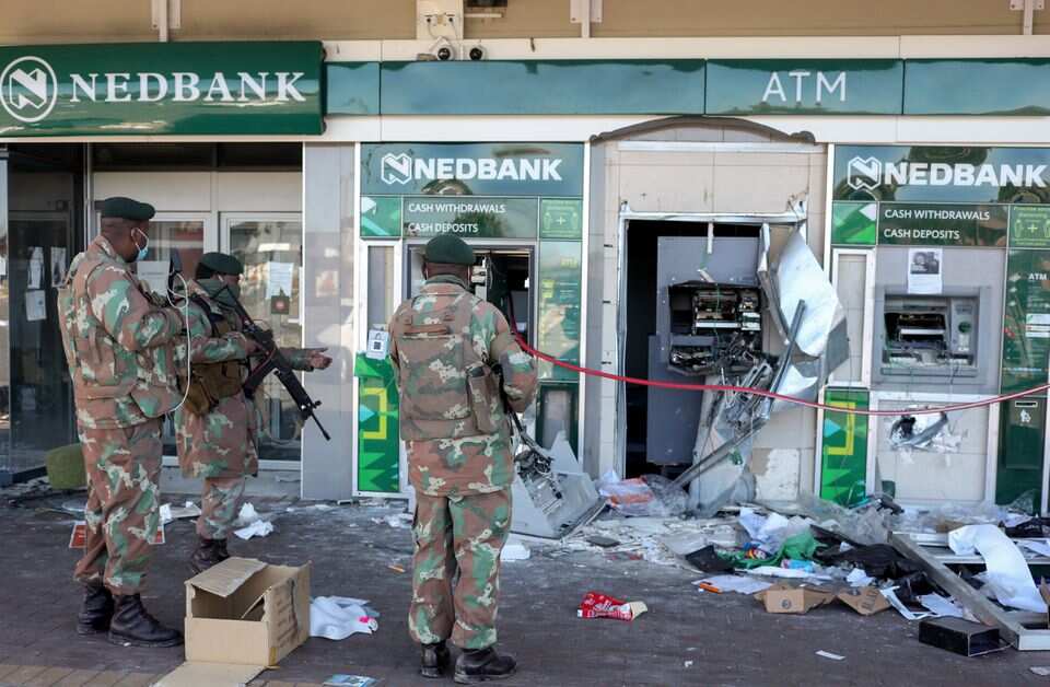 Members of the military look at damaged ATM machines outside a bank as South African riots and looting rage.