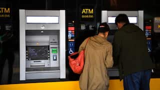 A man and woman wearing a tan jacket stand at a Commonwealth Bank ATM machine.
