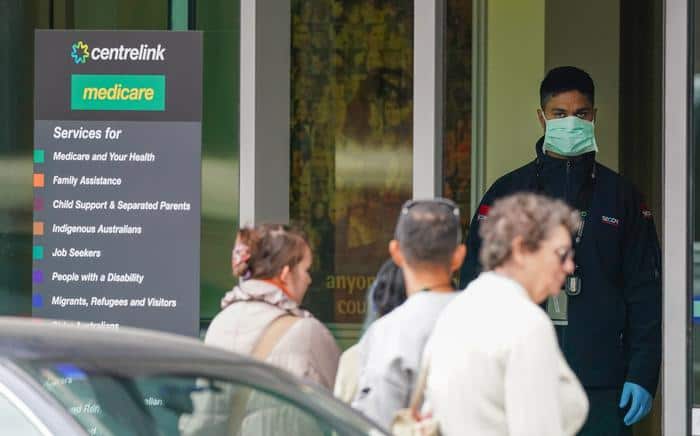 A security guard looks on as people are seen in long queue outside a Centrelink office in Abbotsford, Melbourne, Monday, 23 March, 2020. 