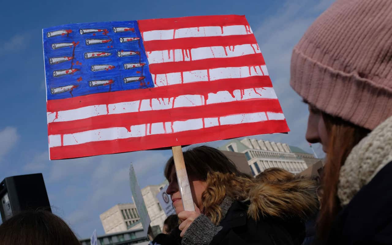 A woman holds a sign with an American flag dripping red and its stars replaced by bullets while protesting at the 'March for our Lives' in Berlin, Germany.