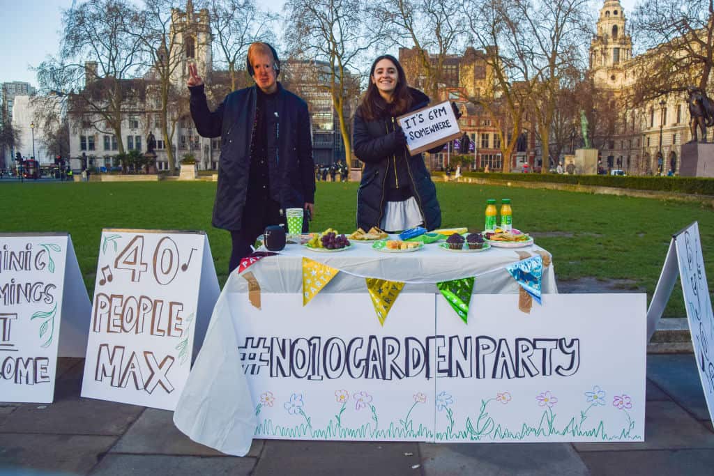 A protester wearing a Boris Johnson mask stands next to the 'No. 10 garden party' table with drinks and snacks during the demonstration at Parliament Square.