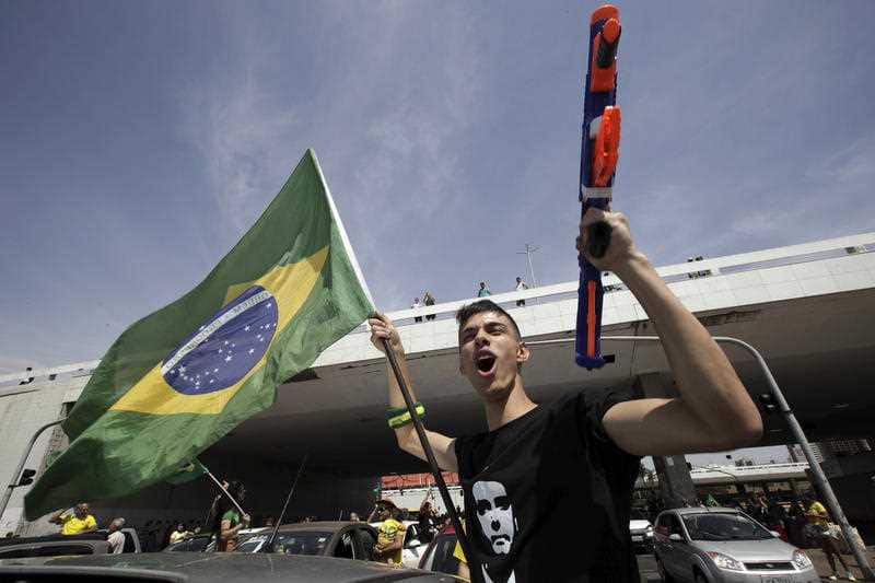 A demonstrator holds a toy gun and a Brazilian flag, during a race in support of Jair Bolsonaro.