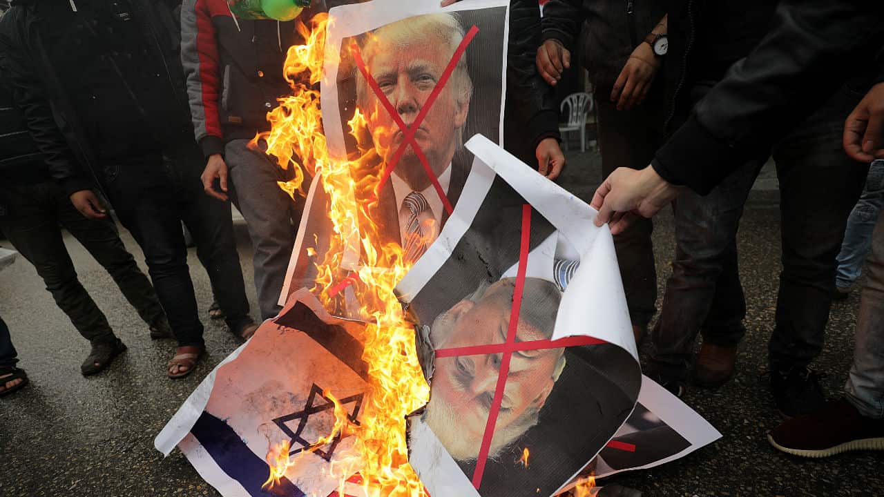Palestinians burn Israeli and US flags and posters of US President Donald Trump and Israeli Prime Minister Benjamin Netanyahu.