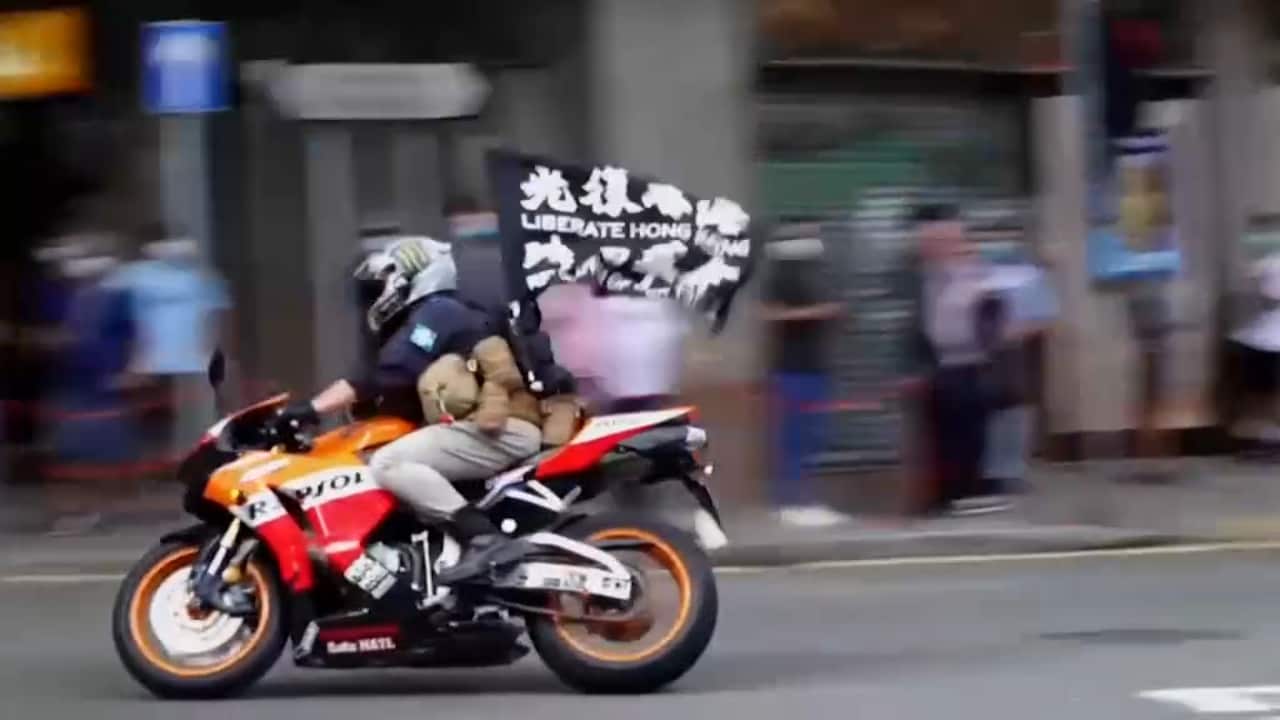 Archive: 1 July 2020, motorcyclist with flag reading (English and Chinese) "Liberate Hong Kong, Revolution of Our Times" accelerating towards police line.