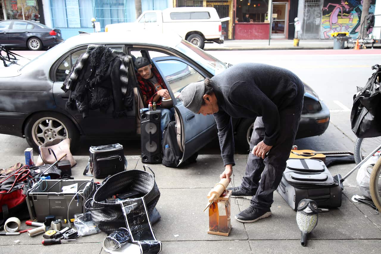 Jake Orta sets out his wares for sale on a sidewalk as his friend, who goes by Yosemite Sam, looks on in San Francisco on Jan. 25, 2019.  