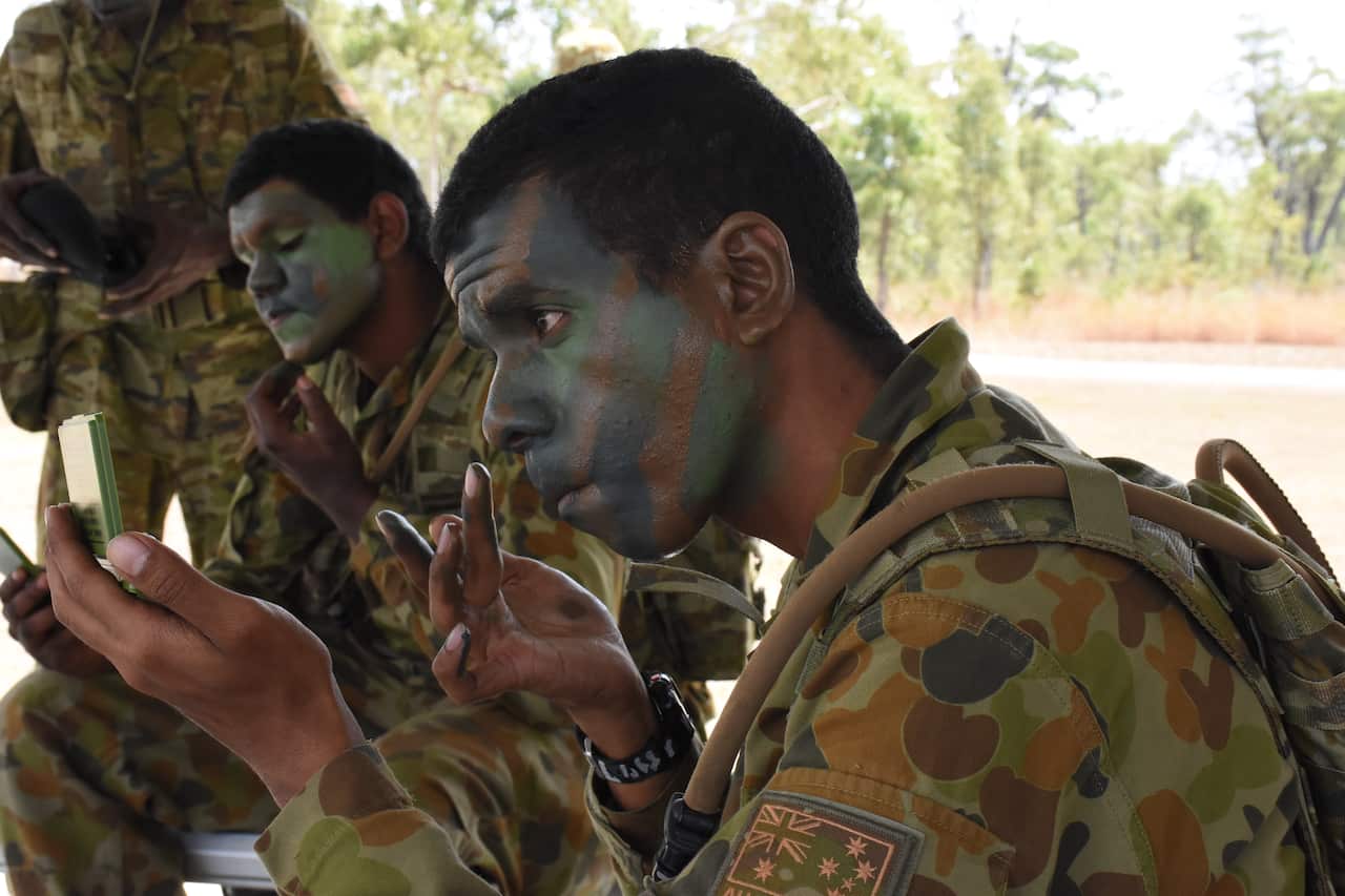 Soldiers apply camouflage paint as part of a lesson on concealment in the bush.