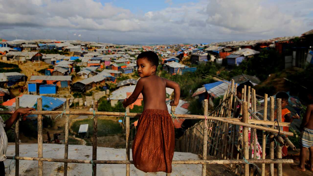 A Rohingya child stands on a bamboo fence overlooking an expanse of makeshift bamboo and tarp shelters at Kutupalong refugee camp.