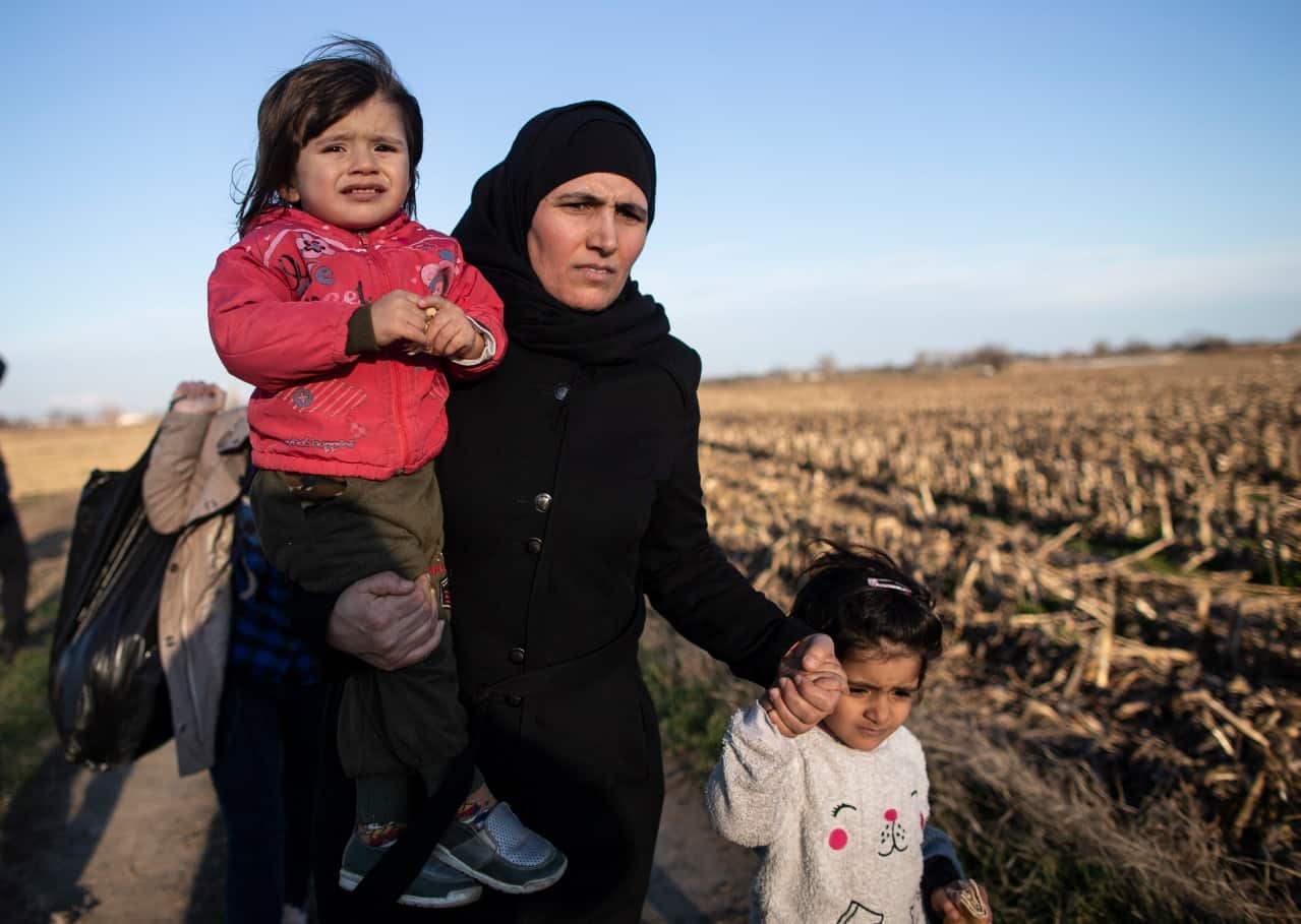 Refugees walk near fences enforcing the Greek border as they try to enter Europe, in Edirne, Turkey, 28 February 2020. 