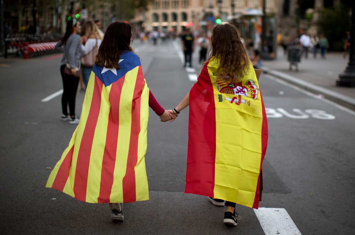 Two teenage girls walk along the street to take part in Tuesday's demonstration. One wears a Spanish flag, while the other wears the independence flag.