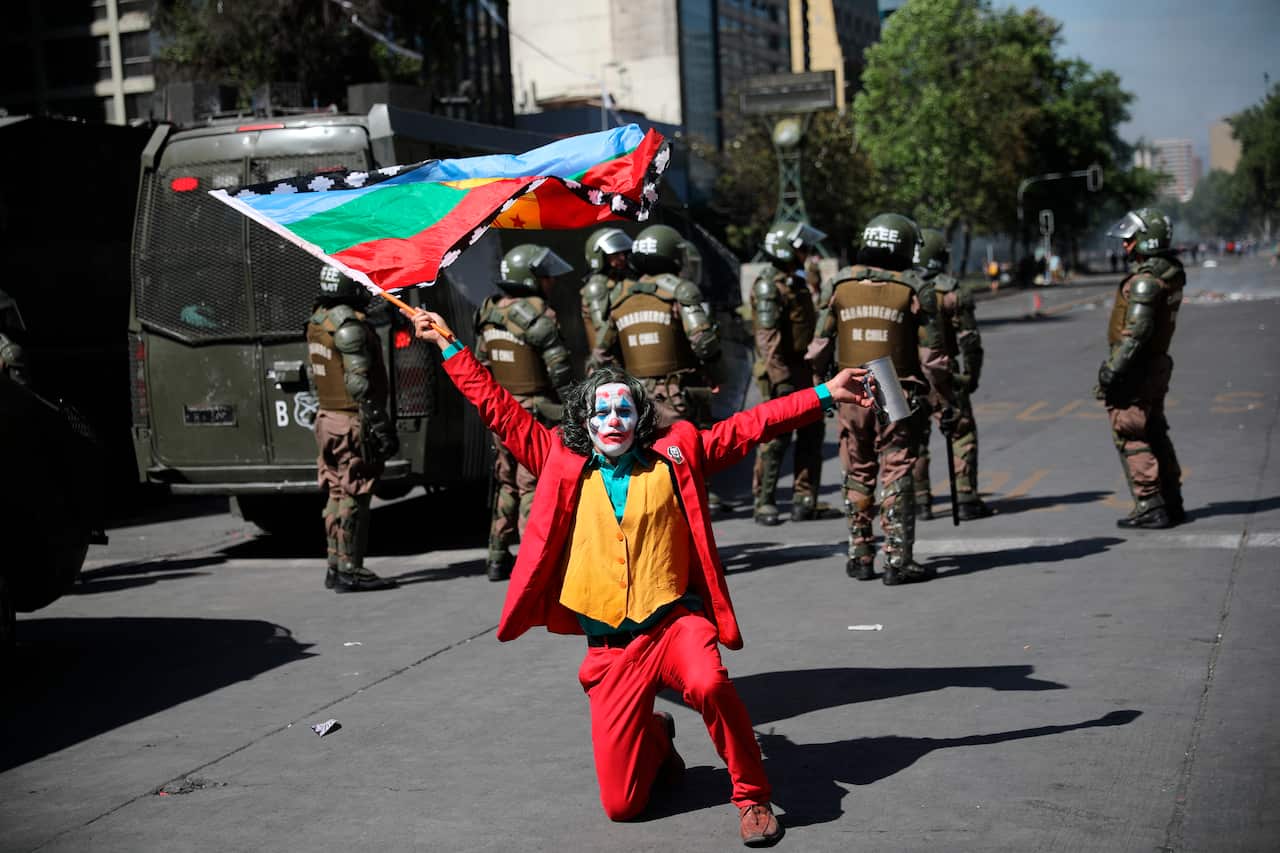 An anti-government protester dressed as the Joker holding a Mapuche flag, strikes a pose in front of police near La Moneda presidential palac.