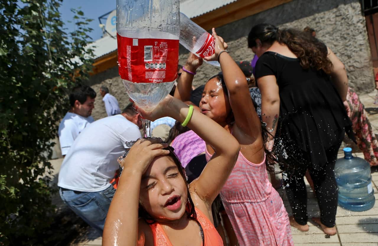 Two girls play refresh themselves while residents gather water from a fire hydrant at a neighborhood in Santiago, Chile, Monday, Feb. 27, 2017. (AAP)