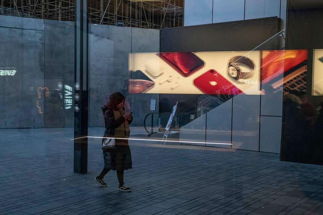 A woman checks her phone while walking past an Apple advertisement, in Beijing.