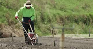A man in a hi vis jacket and a hat is using a traditional tool in a farmland.