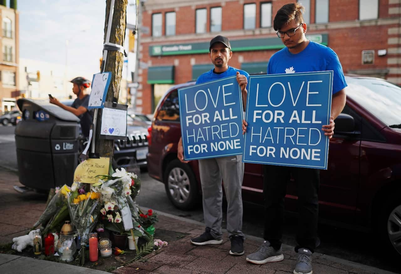 People hold signs at a memorial remembering the victims of Sunday's shooting in Toronto on Monday, July 23, 2018.