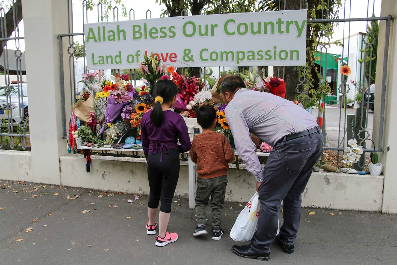 A man and his children place flowers as a tribute outside the Al-Noor Mosque on 15 March 2021. 
