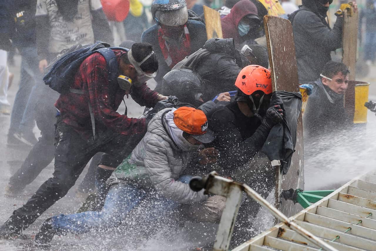 Anti-government protesters take cover from a police water cannon during clashes in Madrid, on the outskirts of Bogota, Colombia.