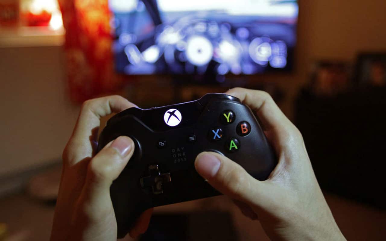 A teenager holding a controller to play a video game on a Microsoft Xbox One console.