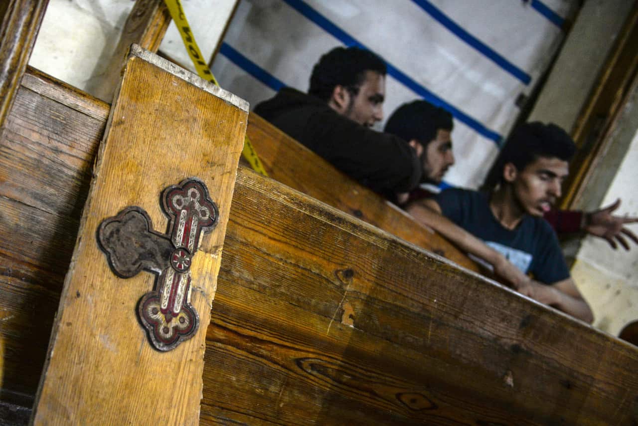 A cut off cross panel lies against a wall as people gather to view the damages at the scene of a bomb explosion inside Mar Girgis church in Tanta. 