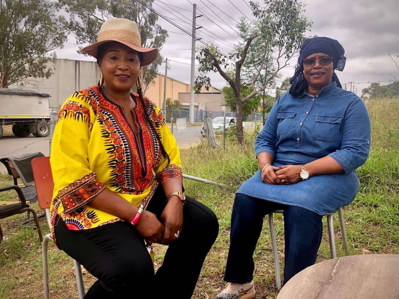 Abie Kallay and Fatma Mansaray sit at table near farm gate.