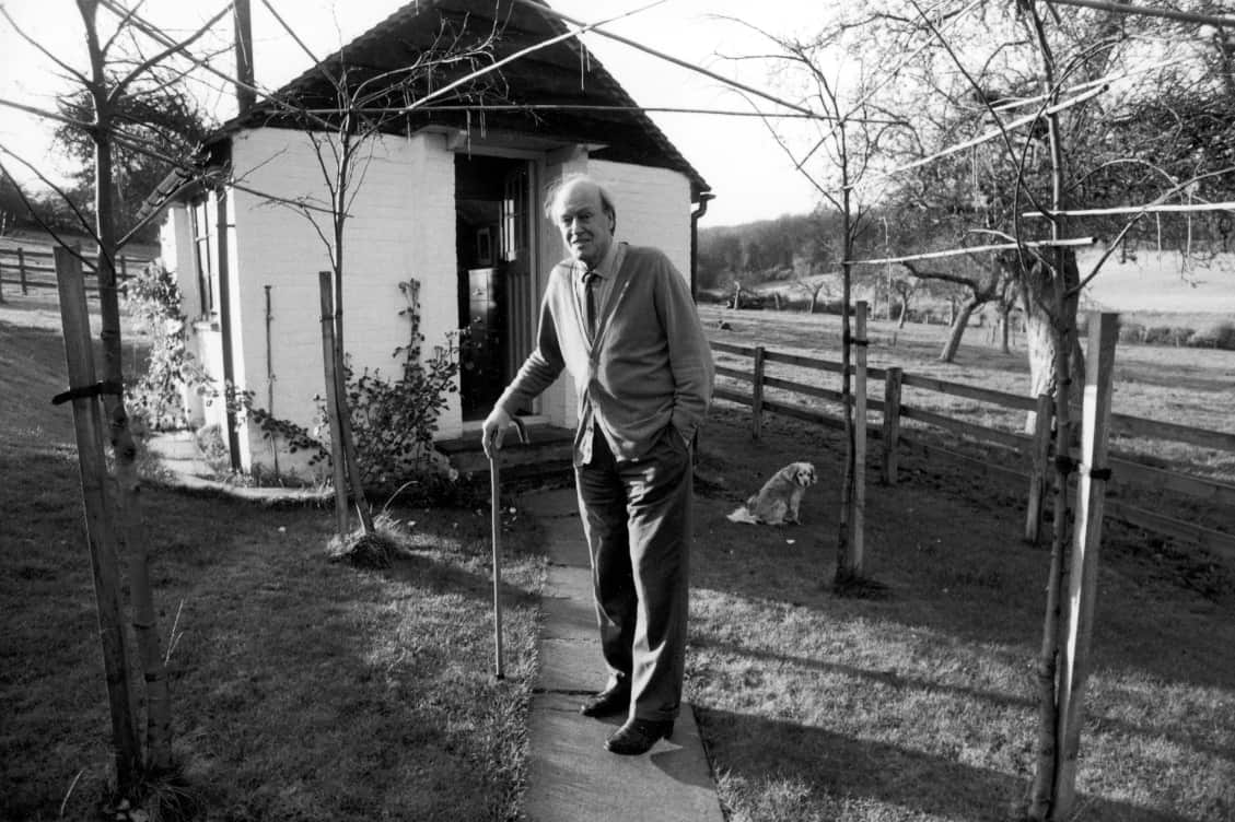 Writer Roald Dahl holds onto his cane while standing outside the shed where he writes.