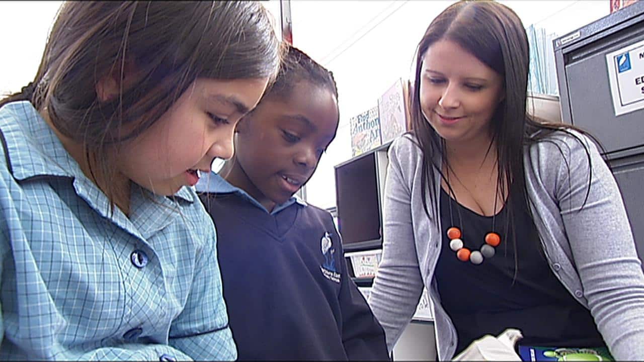 Teacher Chanel Herring sits with students working on their reading lesson (SBS)